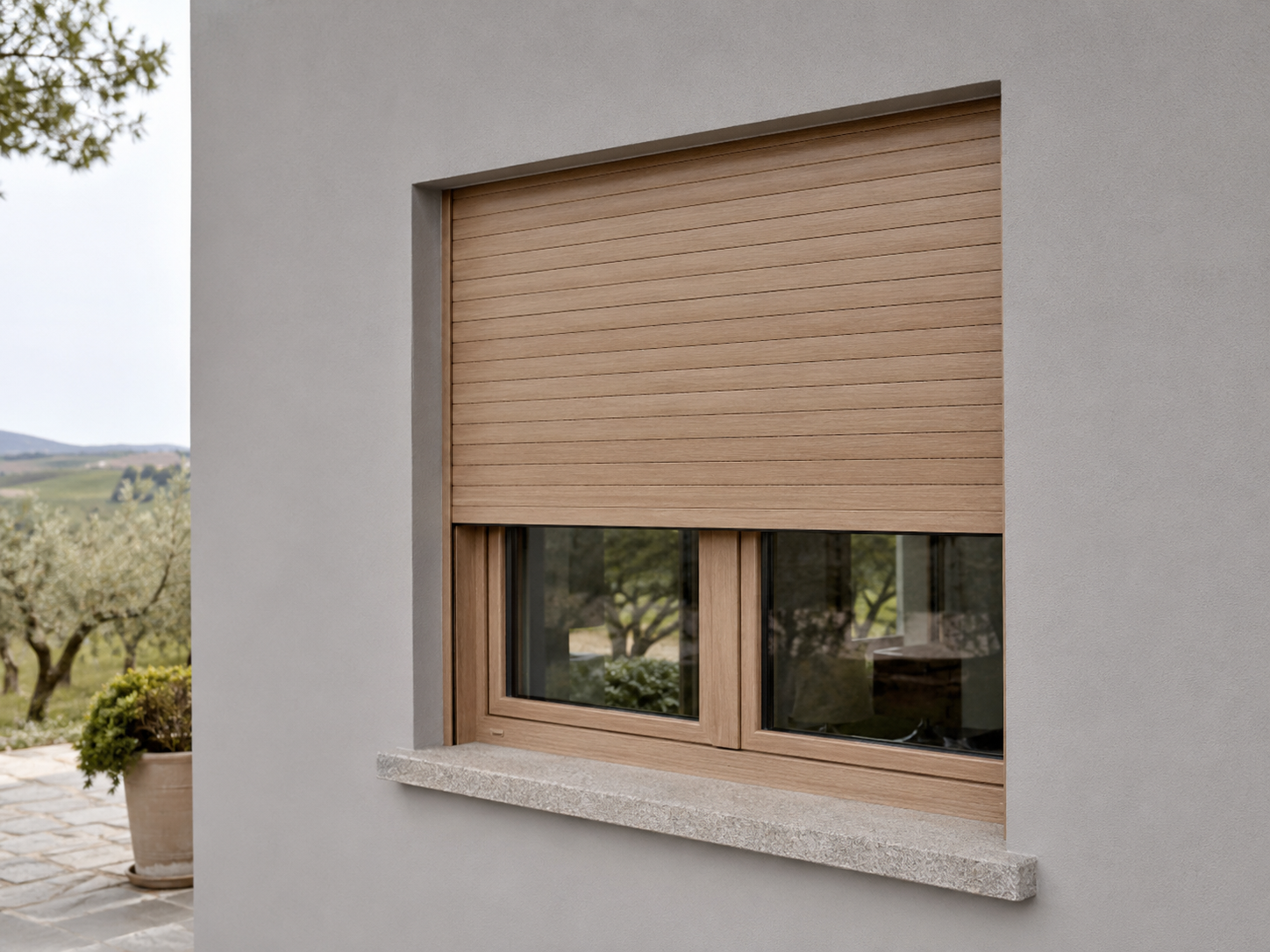 Avvolgibile in alluminio effetto legno rovere chiaro su una finestra con vista collinare e uliveto